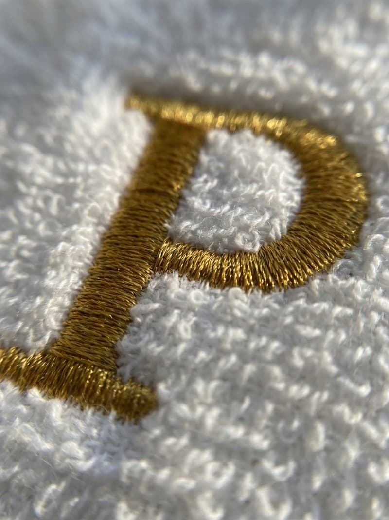 Nahaufnahme einer goldfarbenen Maschinenstickerei auf weißem Frottee